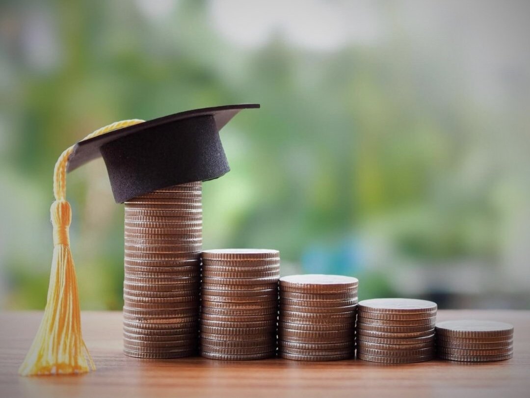Ascending columns of coins with a graduation cap topping the tallest column.
